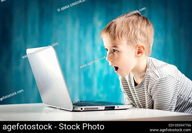 happy five years old child sitting with a laptop at table. Smiling boy working at personal computer