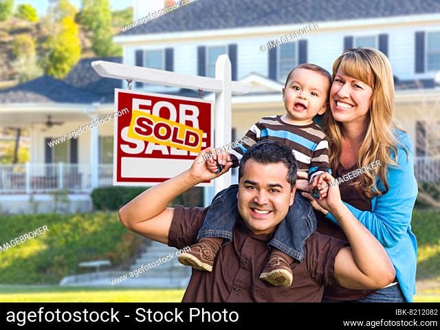 Happy mixed-race young family in front of sold home for sale real estate sign and house
