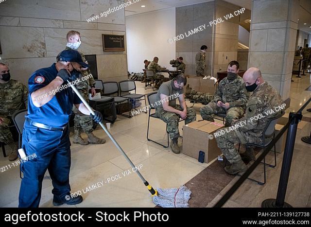 A worker mops the floor while members of the National Guard play cards in the Capitol Visitors Center at the US Capitol, the day after the inauguration of...