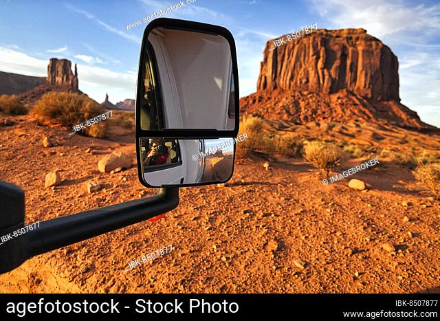 Motorhome on gravel road in front of striking rock formation, West Mitten Butte and Merrick Butte, view in the rear view mirror
