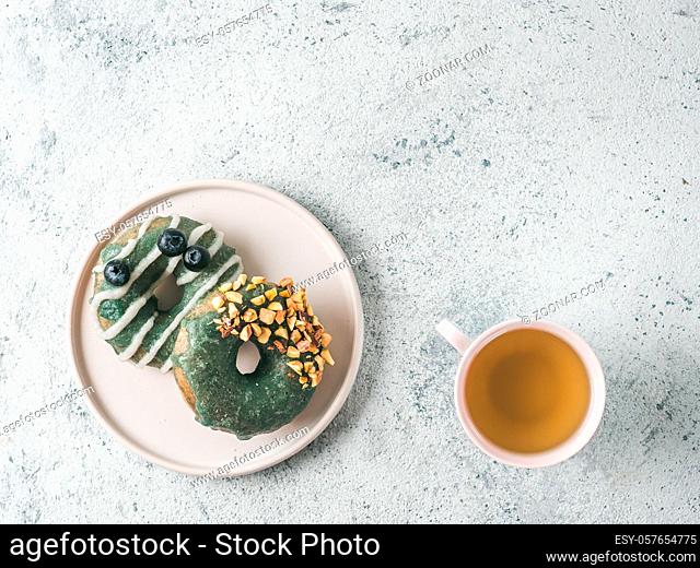 Vegan doughnuts with chia seeds topped with healthy spirulina glaze with pistachio and blueberry. Blue green spirulina donuts and herbal tea cup on gray...