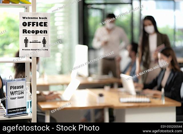 Signage of Office Reopen with social distancing practice with blurred background of Asian team business people working and wear face mask in new normal office...