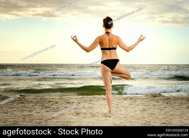 beautiful woman in a black swimsuit practicing yoga on the beach at sunset
