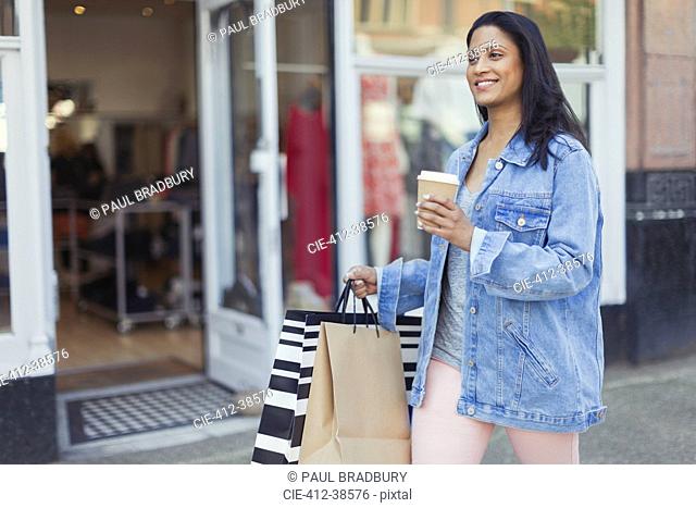 Smiling woman walking along storefront with coffee and shopping bags