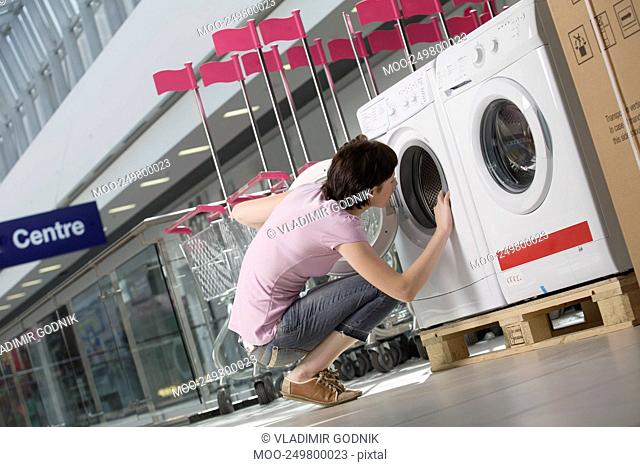 Young woman looks inside tub of washing machine in shopping mall Voronezh