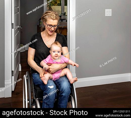 A paraplegic mother holding her baby on her lap while moving around her home in a wheel chair:: Edmonton, Alberta, Canada
