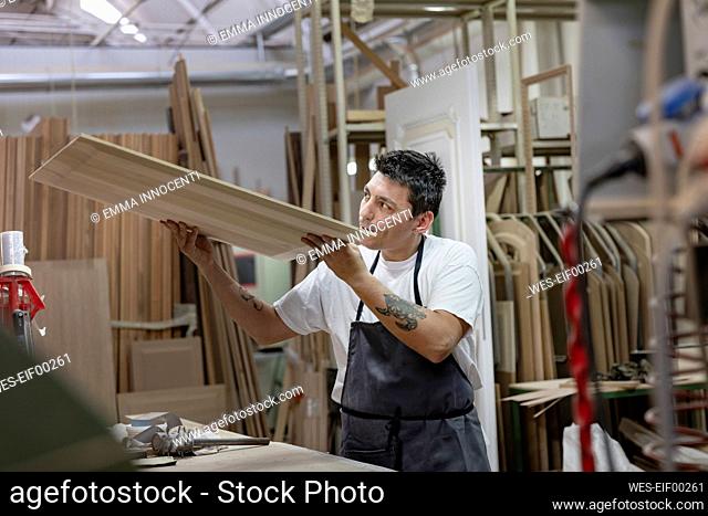 Artist examining wood while standing at workshop