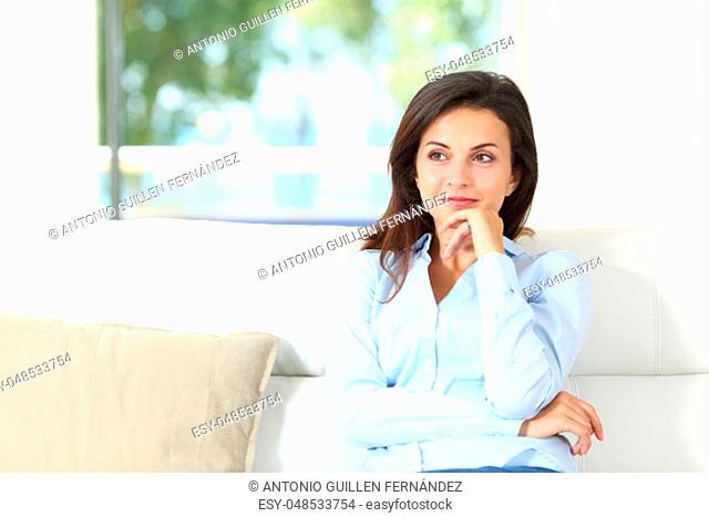 Front view of a pensive homeowner sitting on a couch in the living room at home