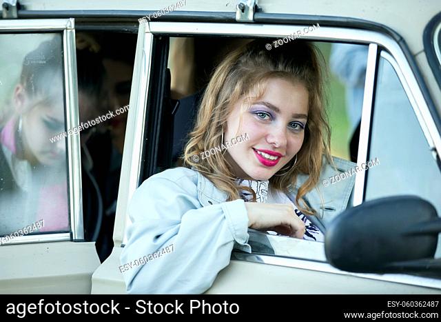 A girl with bright makeup looks out of the window of a retro car