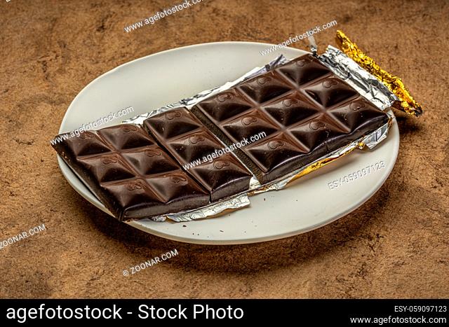 unwrapped and broken chocolate bar on white plate against brown textured paper
