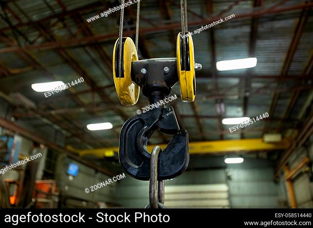 selective focus close up view of lifting hook with safety latch attached to sheaves suspended by wires ropes, factory or workshop interior background