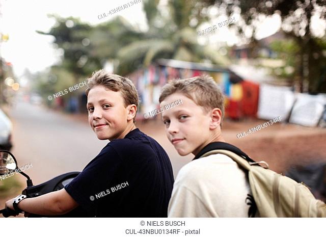 Teenage boys riding scooter on dirt road
