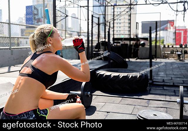 Woman drinking water and relaxing at rooftop gym on sunny day