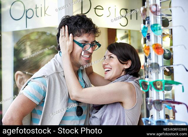 Happy woman trying eyeglasses on boyfriend at store