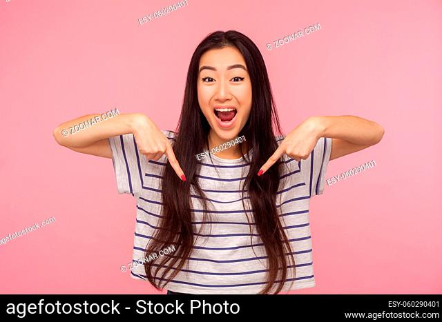 Wow look at advertise, Portrait of excited, surprised girl in striped t-shirt pointing down and looking with shocked face, showing place for commercial