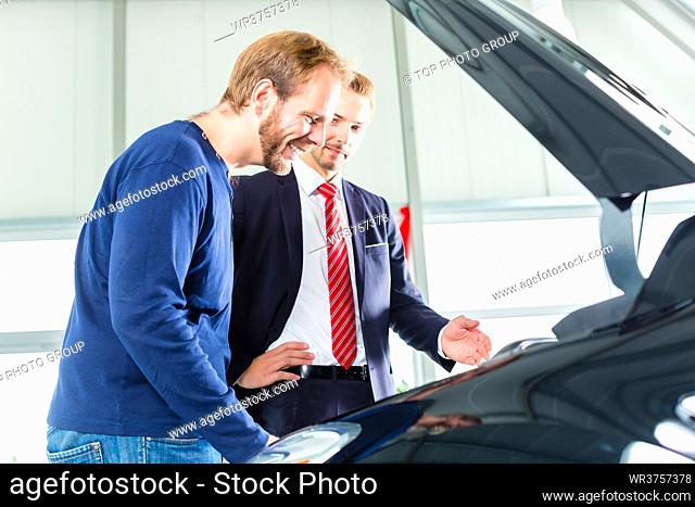 Seller or car salesman and client or customer in car dealership presenting the engine performance of new and used cars in the showroom