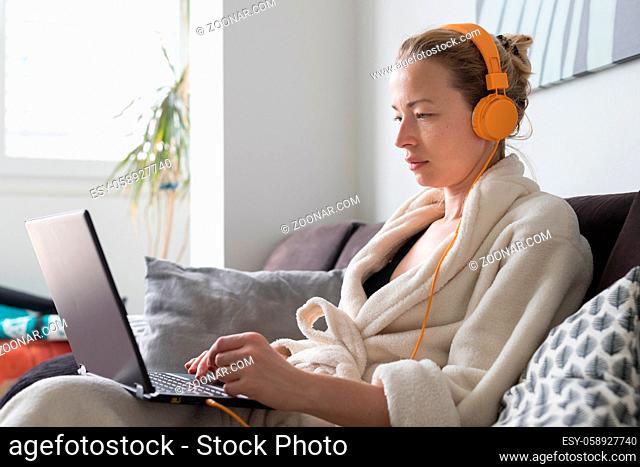 Stay at home and social distancing. Woman in her casual home bathrobe working remotly from her living room. Video chatting using social media with friend