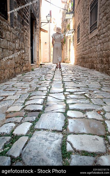 Detail shot of female legs wearing comfortable travel sandals walking on old medieval cobblestones street dring sightseeing city tour