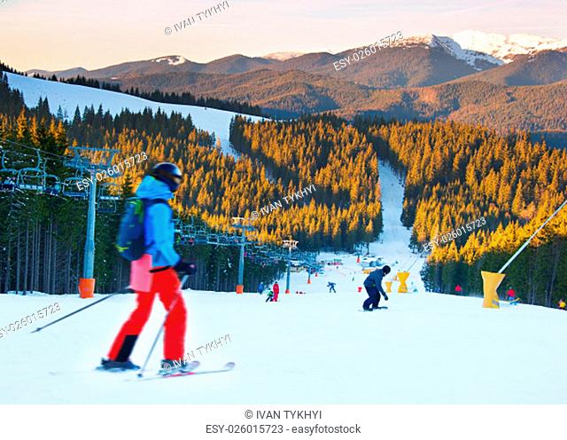 People on a mountains slope at ski resort at sunset