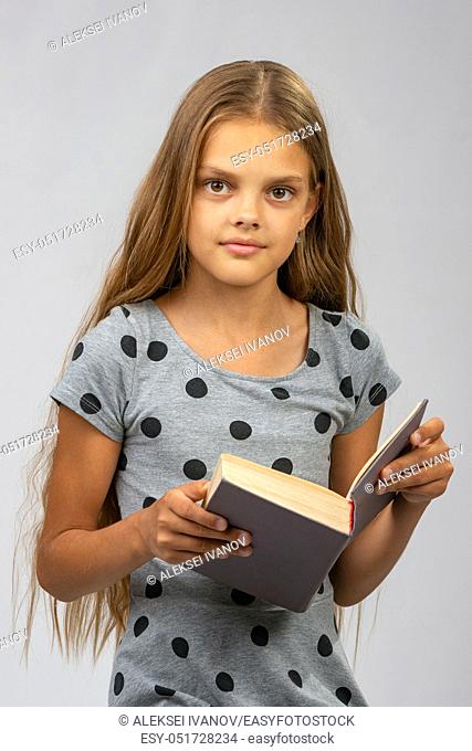 Beautiful ten year old girl reads a book and looks into the frame