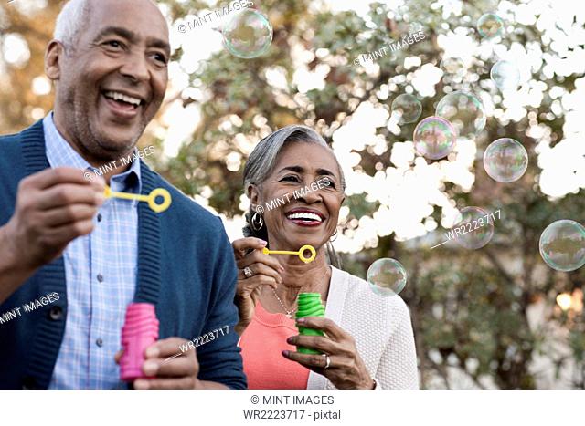 A mature couple, man and woman blowing bubbles celebrating an occasion outdoors