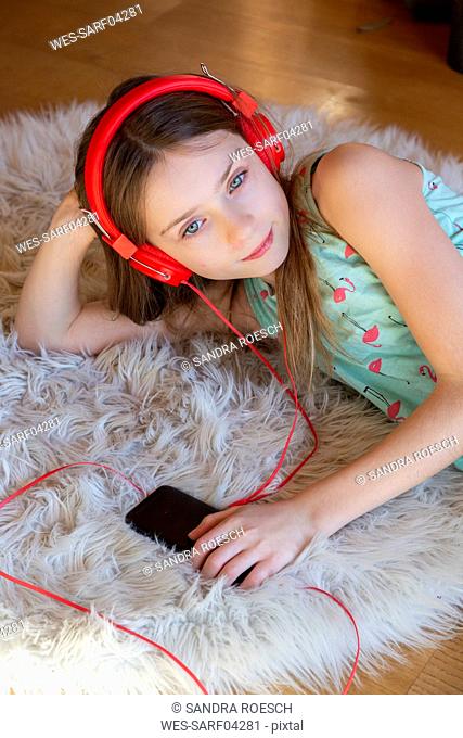 Girl lying on carpet at home listening to music with headphones and smartphone