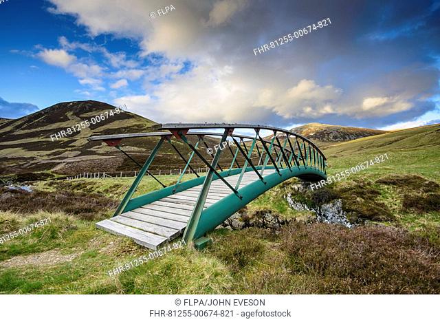 Metal footbridge over river in glen, in evening sunlight, Clunie Water, near Braemar, Cairngorms N.P., Aberdeenshire, Highlands, Scotland, May
