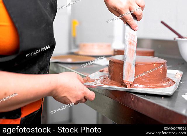 Woman pastry chef finishing chocolate cake with icing, final stage of cooking. The process of making the chocolate cake. High quality photo