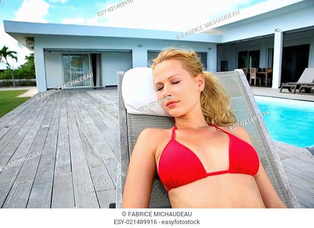 Blond woman in red bikini relaxing by pool