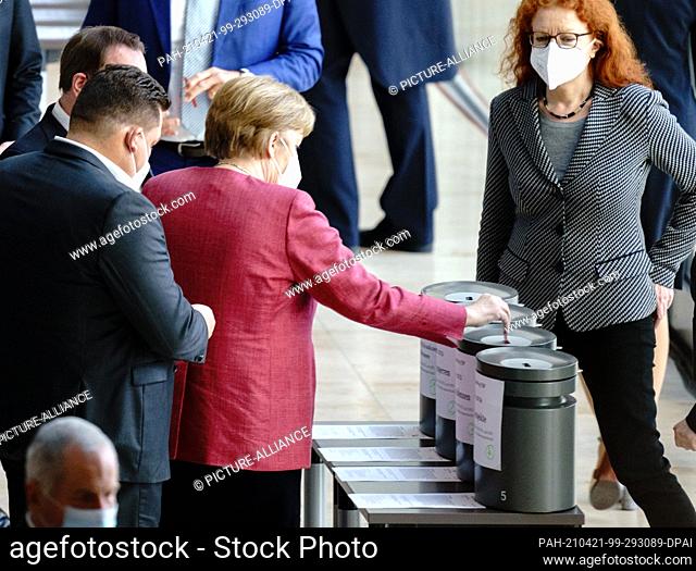 21 April 2021, Berlin: Chancellor Angela Merkel (CDU) hands in her voting cards during the vote on amendments at the Bundestag session