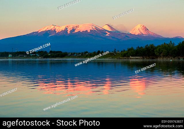 Sunset lighting Kluchevskaya group of volcanoes with reflection in the river Kamchatka