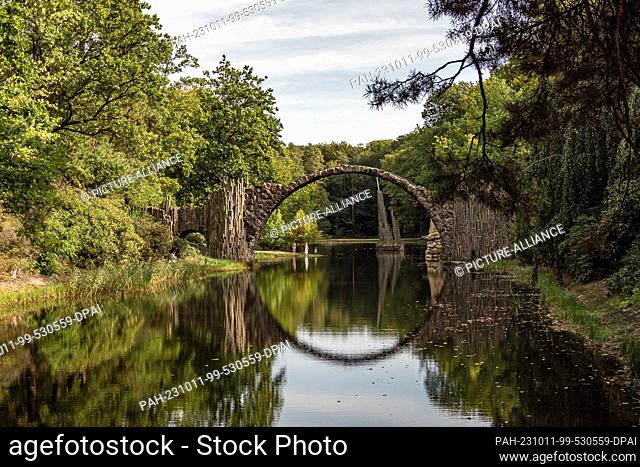 11 October 2023, Saxony, Kromlau: The Rakotz Bridge made of basalt stones in the Kromlau Rhododendron Park is reflected in the Rakotz Lake