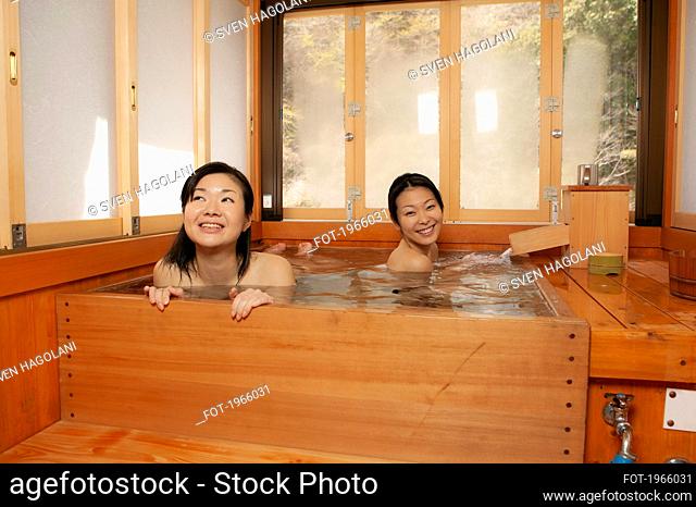 Happy young women friends soaking in wooden pool at Onsen