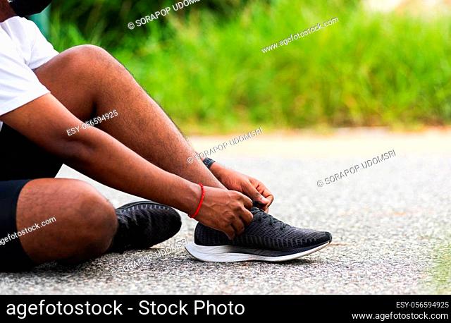 Close up Asian sport runner black man sitting shoelace trying running shoes getting ready for jogging and run at the outdoor street
