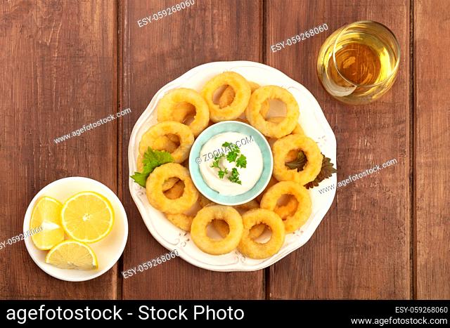 Calamari rings with a mayonnaise dip, lemons, and a glass of wine, shot from above on a dark rustic wooden background with copyspace