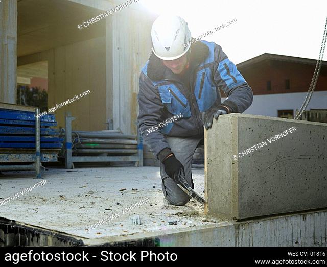 Worker cleaning corner of cement slab with hammer kneeling at construction site
