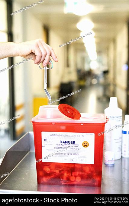 19 December 2019, Baden-Wuerttemberg, Freiburg: An employee drops a pair of scissors made of non-reusable medical stainless steel into a container for...