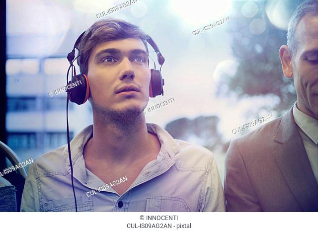 Young man daydreaming and listening to headphones on train
