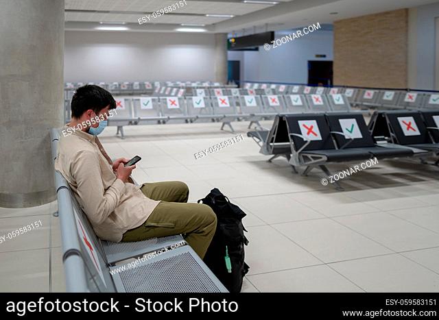 Waiting for flight at empty airport in Cyprus. Man sitting on chair with social distance marker at empty Paphos terminal