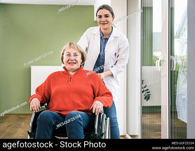 Smiling nurse standing behind woman in wheelchair at home