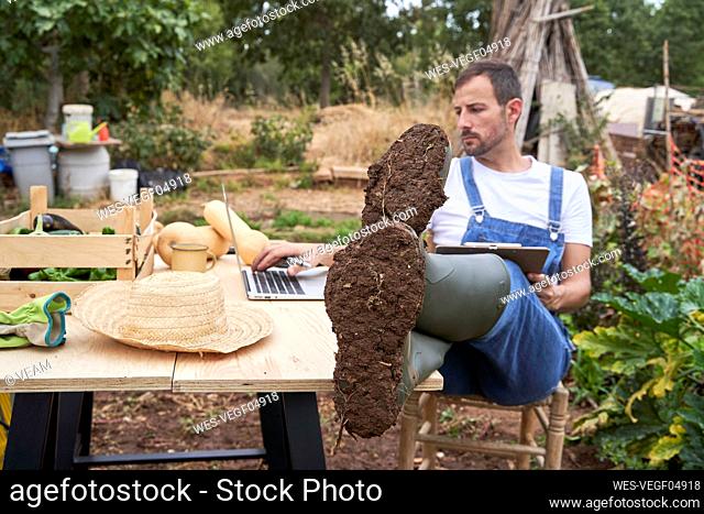 Male farm worker using laptop while sitting with feet up at table in agricultural field