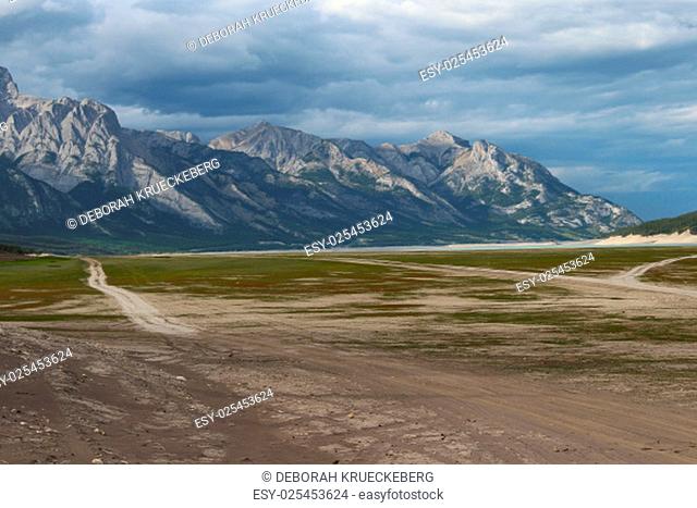 wide field partly green, brown and sandy with skid marks and mountains in the background