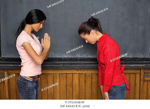 Asian woman bowing in front of an Indian woman
