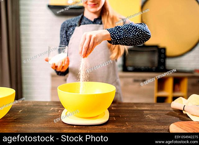 Female person adds sugar into a bowl, cake cooking on wooden table. Fresh tasty dough preparation
