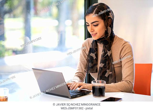Young woman wearing headscarf using laptop in a cafe