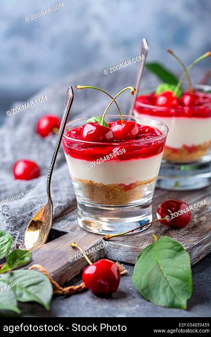 Glasses with cherry cheesecake on an old wooden serving board and dessert spoons on a textured gray background, selective focus