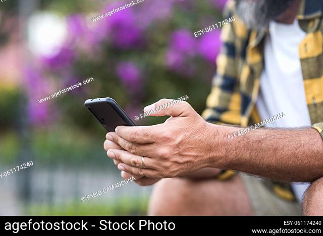 Close up of mature man hands typing and writing on a mobile phone. Male hands people using app on smartphone outdoor. Concept of online dating and wireless free...