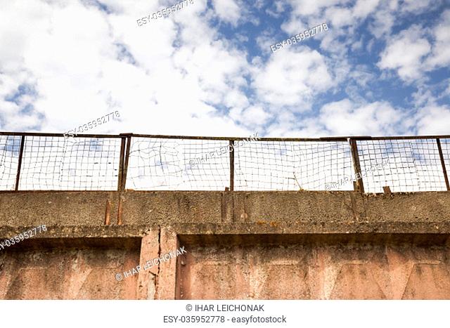 Part of the fence with a metal mesh on top. blue sky. The old part of the building and the fencing of the territory
