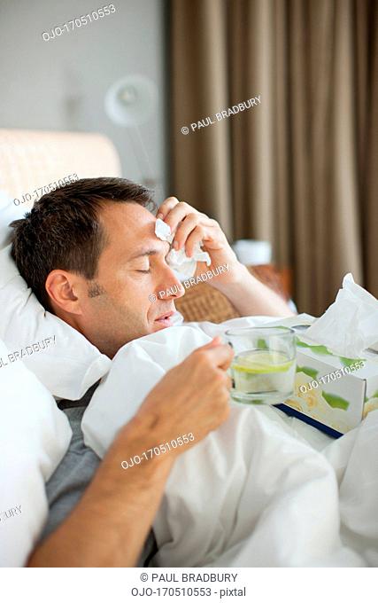 Man sick in bed drinking hot drink