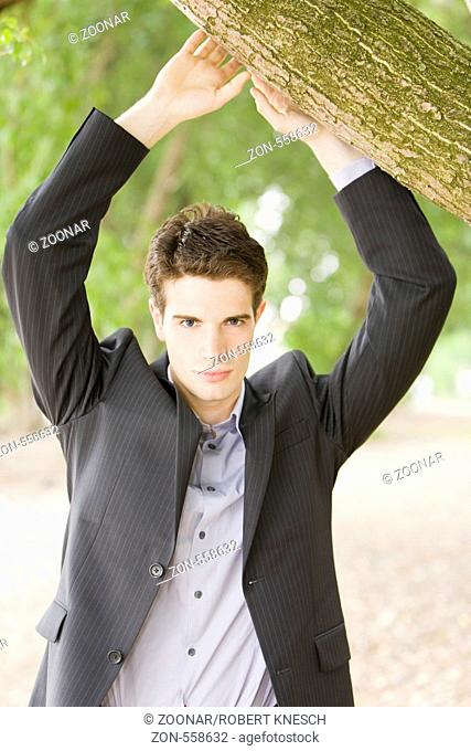 Junger Geschäftsmann steht im Park unter einem Baum